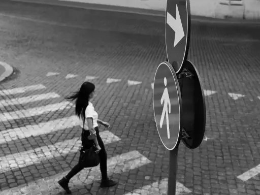 Donna attraversa la strada, un momento catturato con la street photography tecnica. Segnali stradali indicano la direzione.