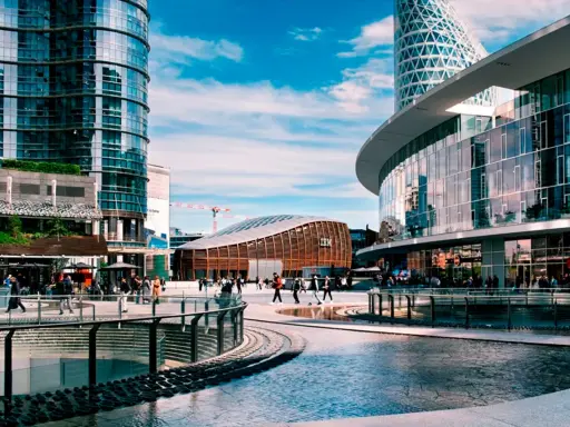 Un'area urbana moderna con grattacieli di vetro, un edificio curvo con il logo IBM e persone che passeggiano. Street photography esempi di vita cittadina.