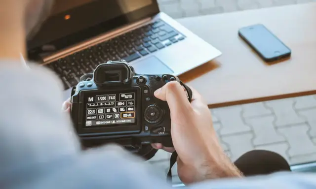 Una foto sera con una fotocamera reflex, un laptop e uno smartphone sul tavolo.