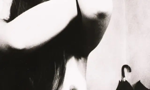 Un corpo femminile in primo piano, con le braccia sollevate, in uno stile che ricorda Bill Brandt. Un ombrello nero è appeso sullo sfondo.