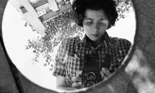 La fotografa famosa si riflette in uno specchio, impugnando la sua macchina fotografica.