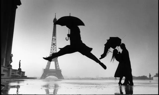 Parigi piovosa: un ballerino salta, una coppia si abbraccia sotto un ombrello. Un'iconica scena che ricorda i grandi fotografi famosi.