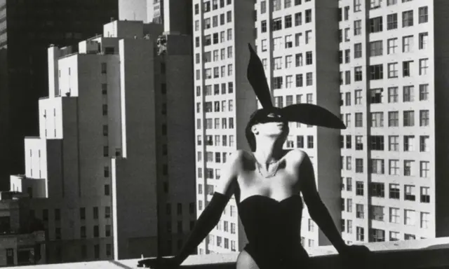 Iconica immagine di Helmut Newton: una donna con orecchie da coniglio e un corsetto nero posa su un tetto, con grattacieli sullo sfondo.