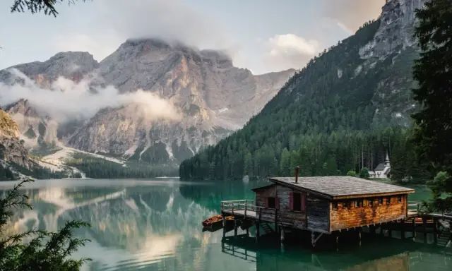 Un rifugio di legno su un lago alpino, perfetto per fotografare paesaggi mozzafiato. Montagne imponenti e foreste verdi incorniciano la scena.