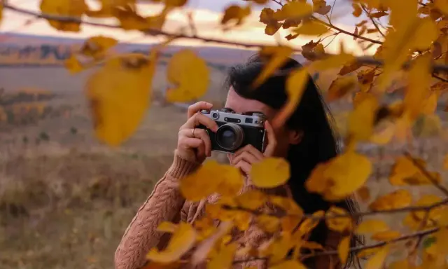 Ragazza con macchina fotografica vintage, tra foglie autunnali. Un tutorial fotografia per catturare la magia della natura.