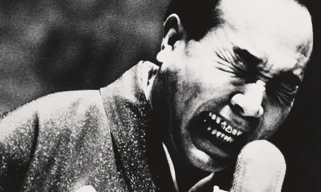 Un uomo con gli occhi chiusi e la bocca spalancata in un grido, un'espressione intensa catturata da Daidō Moriyama.