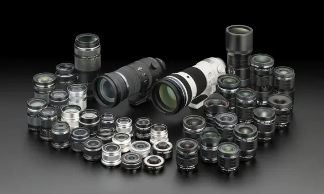 Una vasta collezione di obiettivi fotografici, dai più compatti ai teleobiettivi professionali, disposti su sfondo nero.