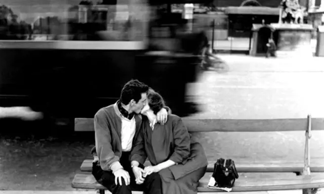 Un bacio rubato tra le opere di Robert Doisneau, un momento sospeso nel tempo con un tram sfocato sullo sfondo.