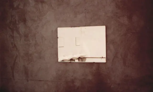 Specchio riflette lavandini in un bagno spoglio, un'immagine che evoca la poetica di Luigi Ghirri.