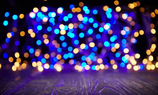 Luci sfocate blu e dorate creano un'atmosfera magica su uno sfondo scuro e un piano in legno viola.
