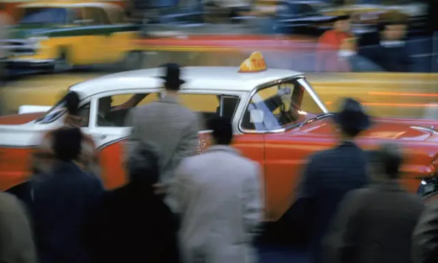Un taxi rosso e bianco sfreccia in una strada trafficata, un'istantanea che cattura l'essenza di quando nasce la fotografia a colori.