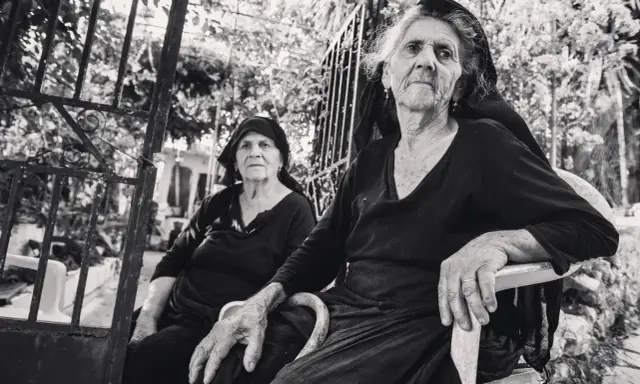 Due anziane donne, ritratte con la sensibilità di Paul Strand, siedono all'aperto, con sguardi intensi e mani segnate dal tempo.