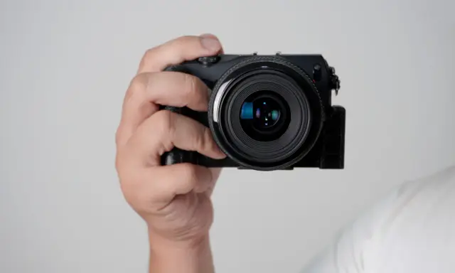 Mano che tiene una fotocamera compatta, mostrando le parti macchina fotografica come l'obiettivo e il corpo nero.