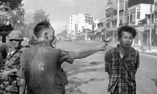 Un soldato punta una pistola alla testa di un uomo in un crudo reportage di guerra. La scena è ambientata in una strada urbana.