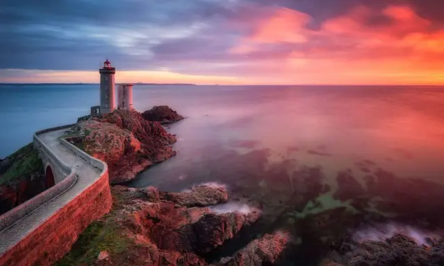 Faro su scogliera al tramonto, con cielo infuocato e mare calmo. Un filtro polarizzatore a cosa serve? A rendere i colori più vividi e il cielo più profondo.