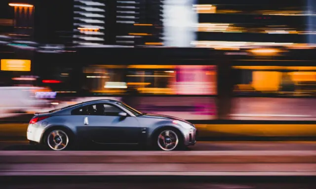 Auto sportiva grigia in movimento notturno, con luci sfocate sullo sfondo che creano un effetto di panning.