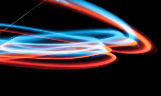 Linee luminose blu e arancioni danzano su sfondo nero, un'esplosione di **light painting** astratto.