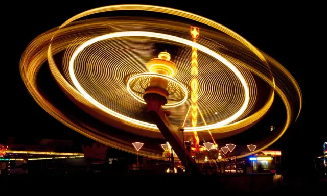 Effetto spirale di luci dorate su un'attrazione da luna park in movimento, catturata con una **panning shot** notturna.