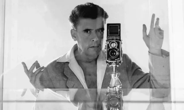 Herbert List si scatta un autoritratto con la sua Rolleiflex, un'immagine iconica che cattura il suo sguardo intenso e le mani in gesto.
