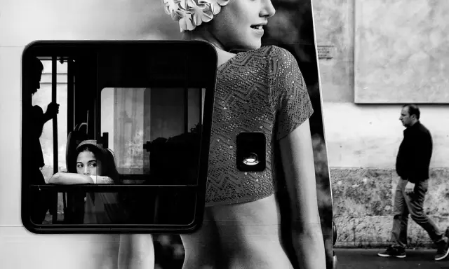 Un uomo cammina mentre una giovane donna guarda fuori da un finestrino. Un'immagine che evoca i grandi fotografi contemporanei.