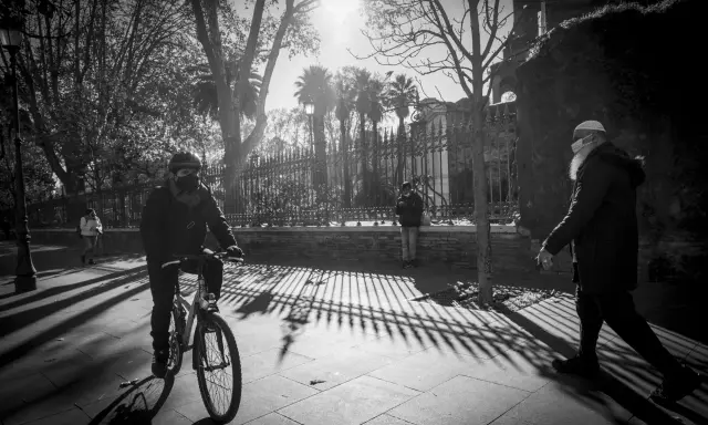 Ombre lunghe e un ciclista mascherato, in uno stile che ricorda robert doisneau, passeggiano sotto il sole.