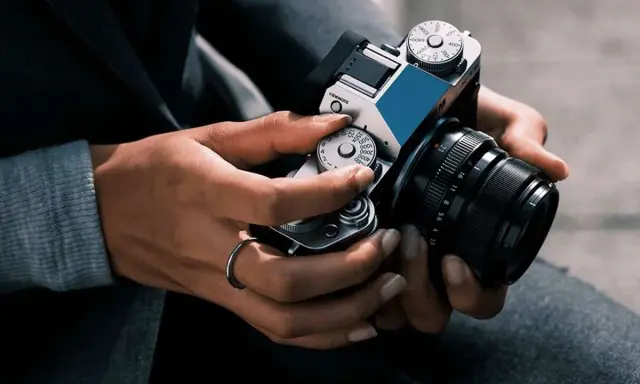 Mani che regolano i quadranti di una fotocamera, con un anello al dito. Immagine fotografica.