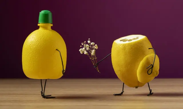 Un limone con un fiore in mano offre un dono a un altro limone. Un esempio di still life che gioca con forme e colori.
