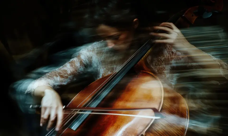 Donna suona il violoncello con un effetto mosso, quasi etereo. Un esempio di come fare foto mosse con iPhone per un risultato artistico.