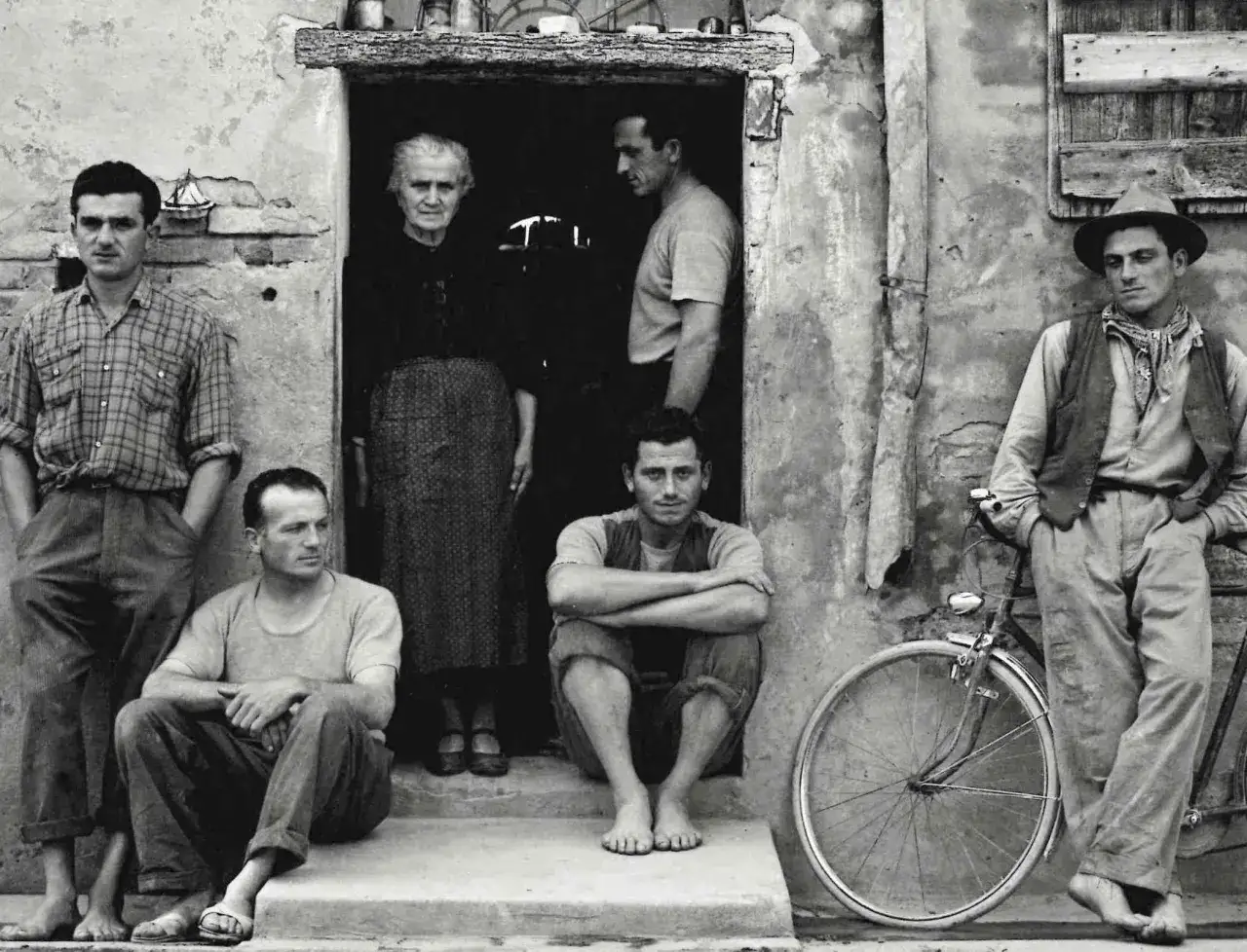 Un ritratto di famiglia di Paul Strand: sei persone posano davanti a una casa, con una bicicletta appoggiata al muro.