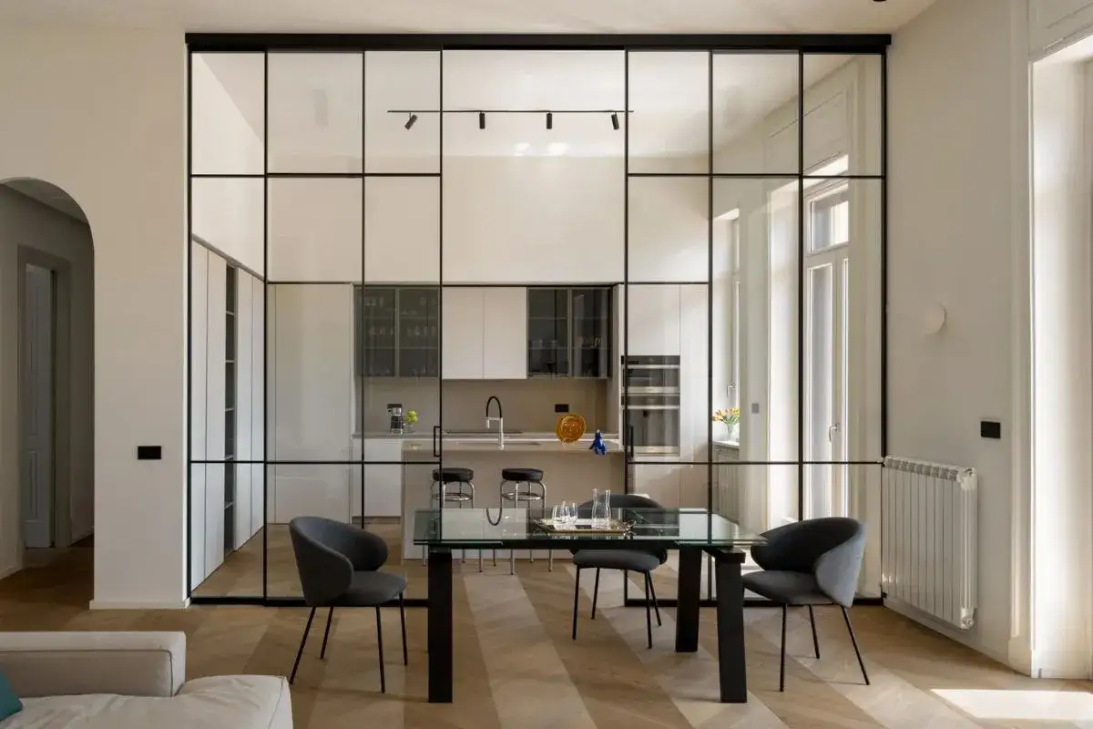 Una cucina moderna e un soggiorno si fondono in questa fotografia minimalista, separati da una parete in vetro con profili neri.