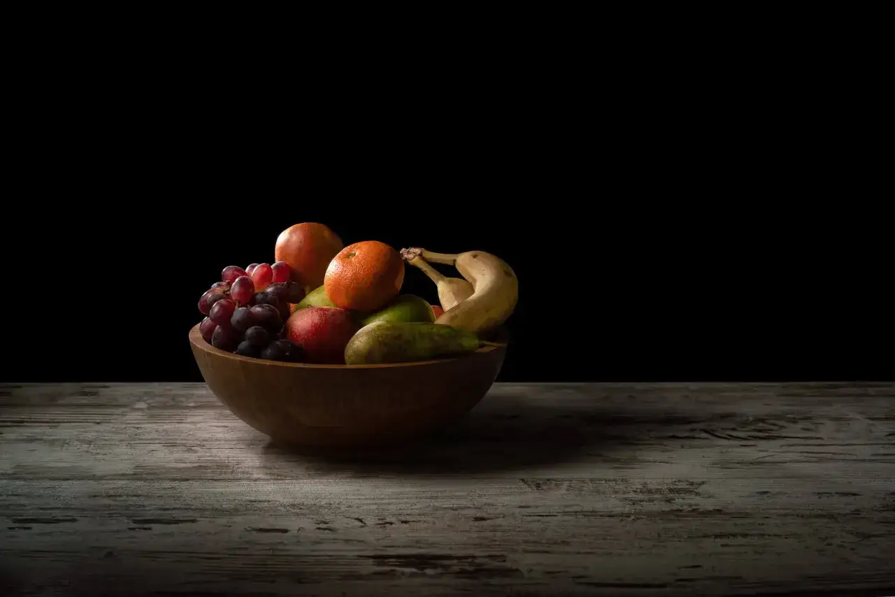 Naturalezza e colore in questa still life fotografia: uva, arancia, mele, pere e banane in una ciotola di legno su un tavolo rustico.