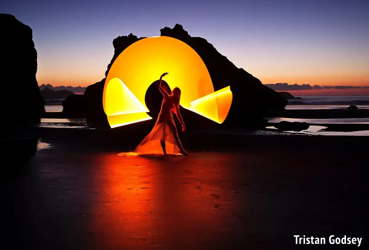 Una figura danzante sulla spiaggia crea un'aura luminosa con il light painting, illuminando il tramonto.