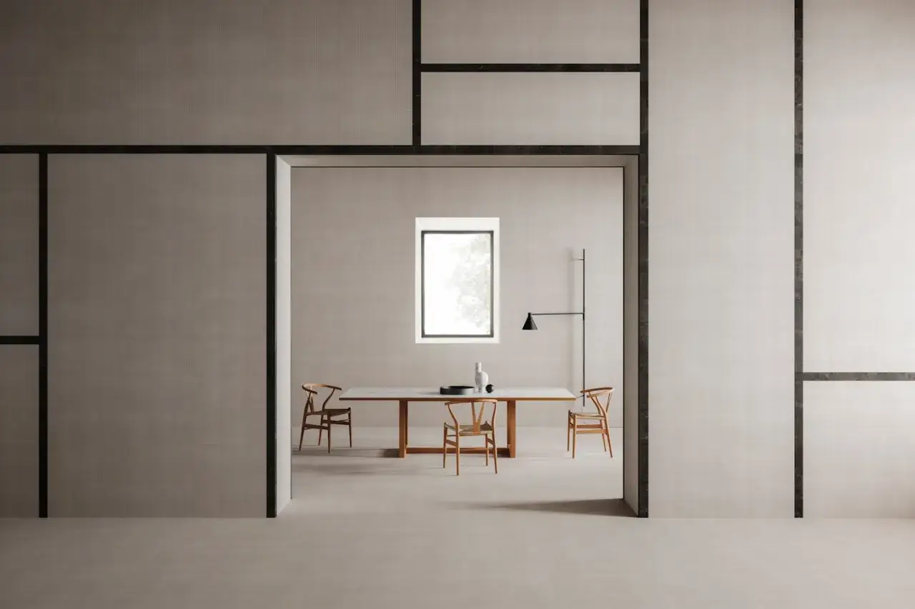 Un'elegante sala da pranzo con tavolo e sedie in legno, illuminata da una finestra. La fotografia minimalista cattura la quiete e la semplicit&agrave; dello spazio.