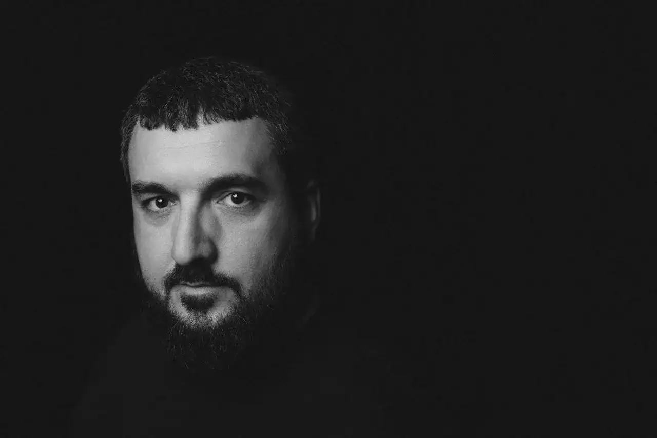 Uomo con barba e capelli corti, primo piano su foto nera sfondo.