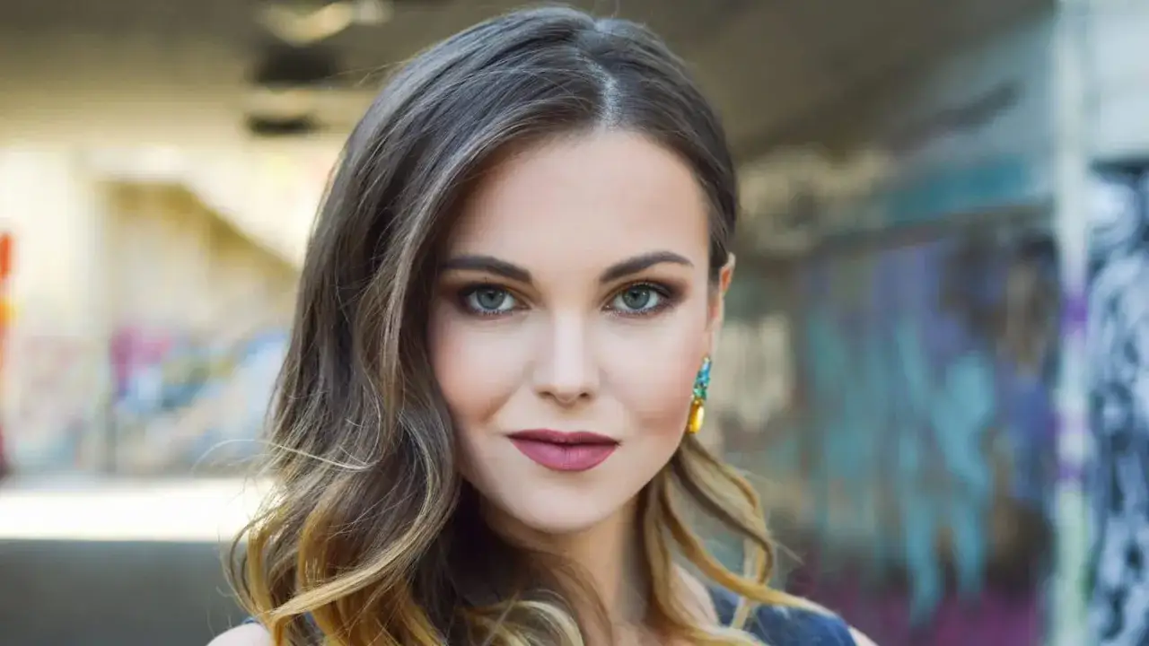 Ritratto di una giovane donna con capelli mossi e trucco marcato, in un ambiente urbano con graffiti. Un fotografo ritrattista famoso cattura la sua bellezza.