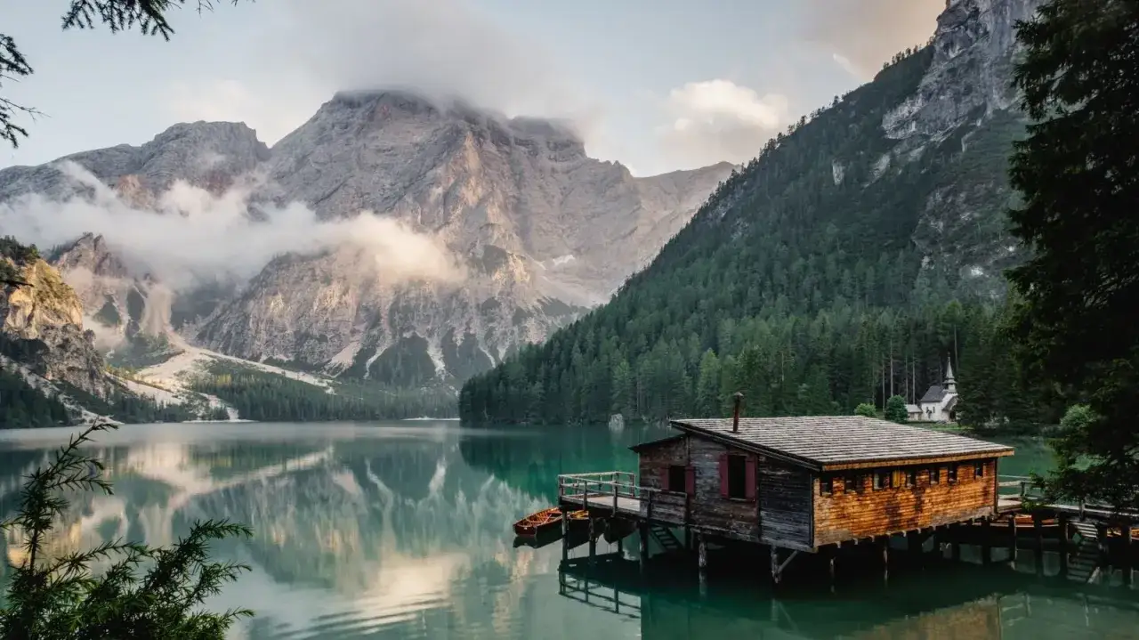 Un rifugio di legno su un lago alpino, perfetto per fotografare paesaggi mozzafiato. Montagne imponenti e foreste verdi incorniciano la scena.