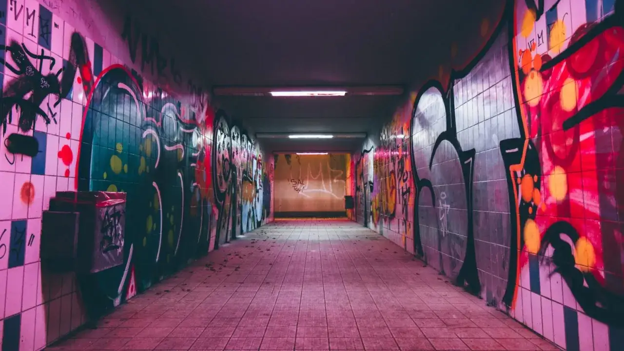 Passaggio sotterraneo illuminato da luci al neon, con pareti ricoperte di graffiti colorati. Un'immagine fotografica che cattura l'essenza urbana.
