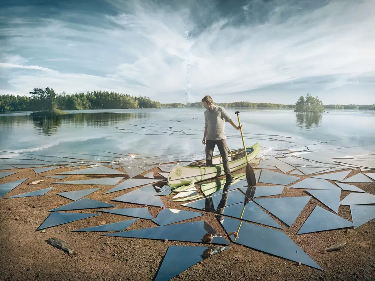 Uomo in canoa su un lago ghiacciato, circondato da frammenti di specchio che creano un surreale foto di reflexo.