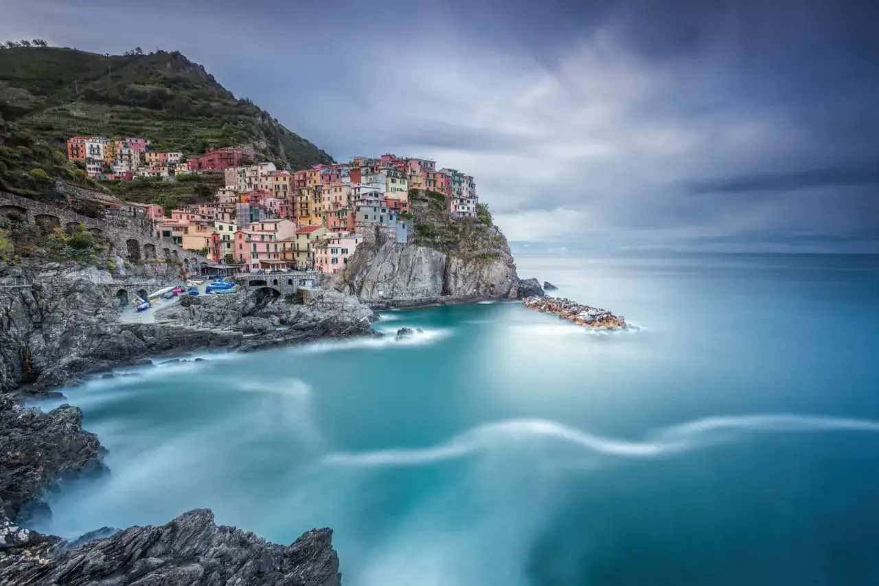 Manarola, Cinque Terre, con case colorate a picco sul mare. L'effetto seta dell'acqua, ottenuto con un filtro ND, crea un'atmosfera magica.