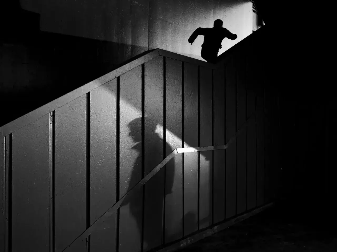 Una figura silhouette corre su una scala, proiettando un'ombra drammatica. Questa foto con ombre cattura un momento di movimento e mistero.