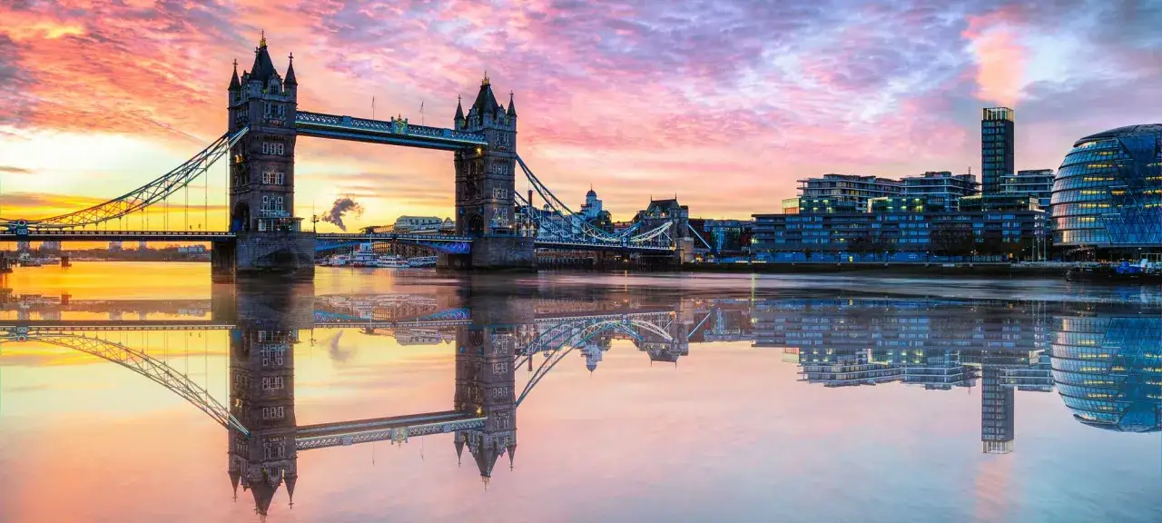 Tower Bridge di Londra al tramonto, con il cielo rosa e arancione che si specchia perfettamente nei riflessi nell'acqua del Tamigi.
