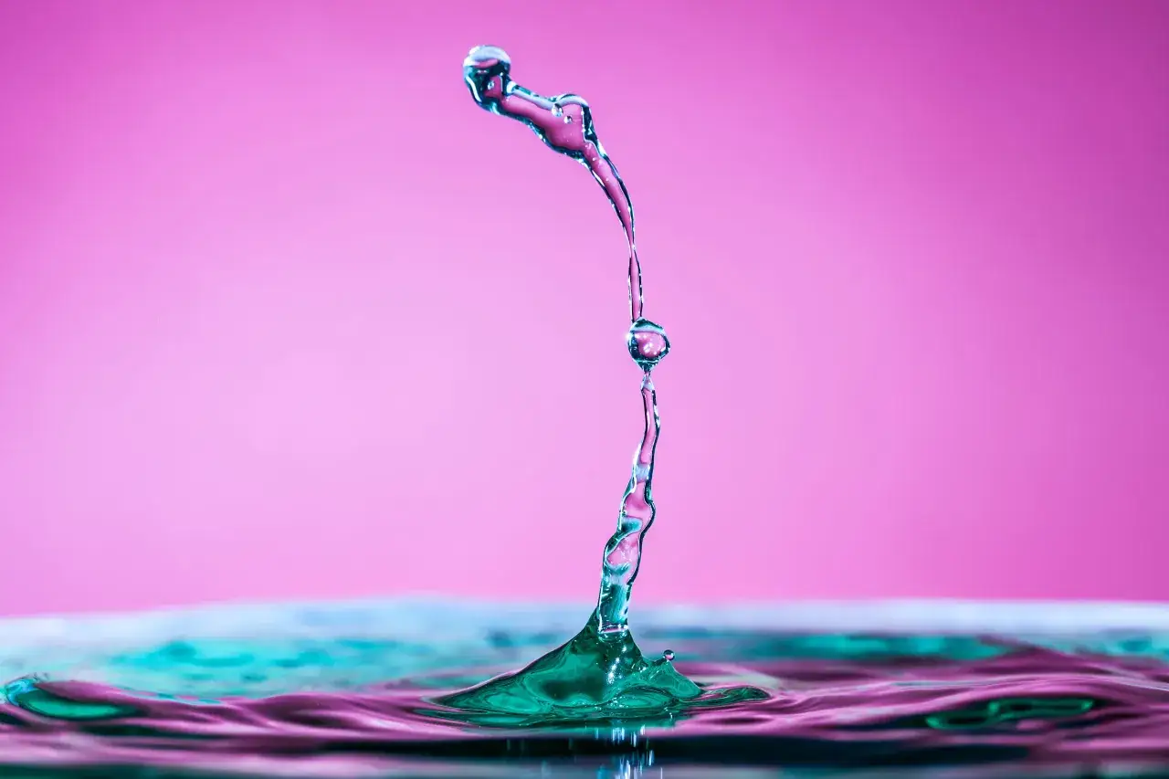 Un getto d'acqua cristallina si innalza, catturato nell'atto di fotografare gocce d'acqua. La luce rosa sullo sfondo esalta le forme liquide.