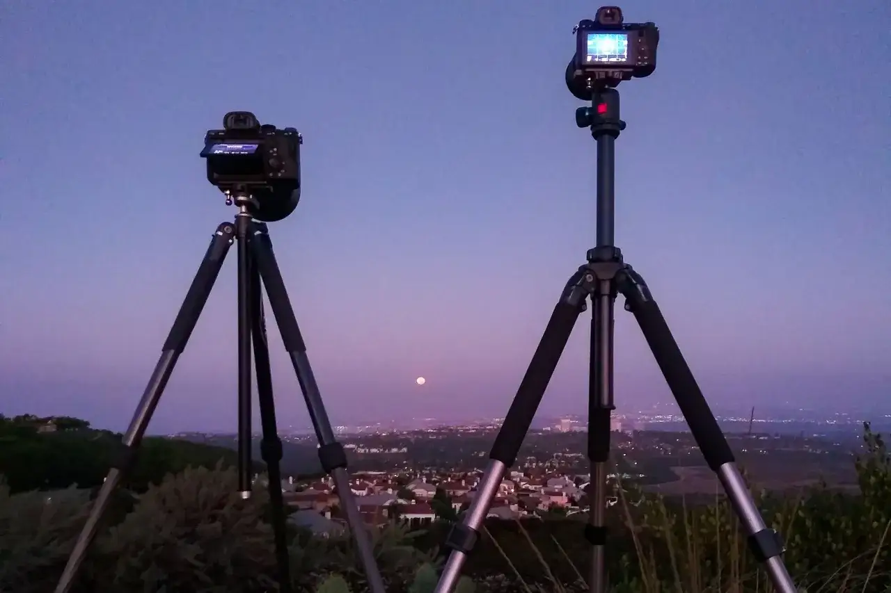 Due fotocamere su treppiedi, pronte per il bracketing fotografia, inquadrano un paesaggio urbano al crepuscolo con la luna piena.