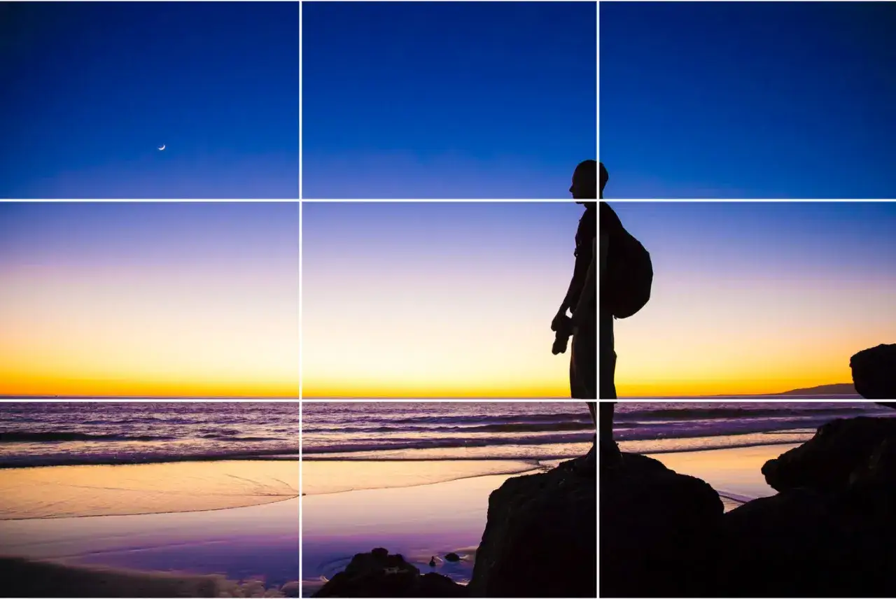 Silhouette di un fotografo sulla spiaggia al tramonto, con la luna crescente nel cielo. La composizione segue la regola dei terzi png.