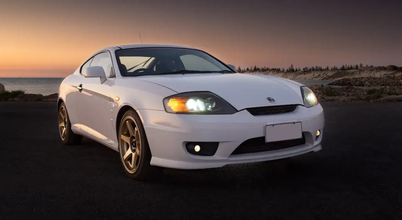 Bianca coup&eacute; sportiva ferma sulla strada al tramonto, con i fari accesi. Un'ottima occasione per fotografare auto ferme in un paesaggio suggestivo.