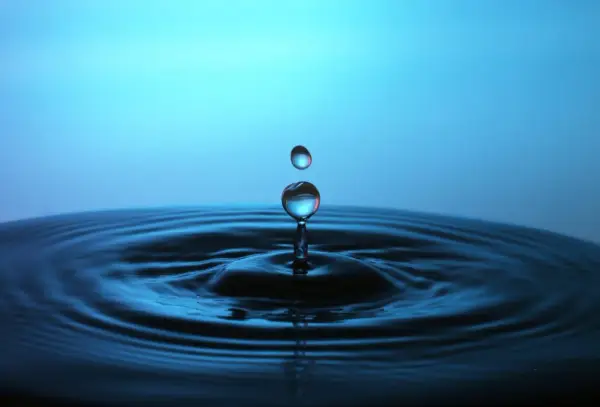 Momento magico nel fotografare gocce d'acqua: una cade, l'altra la segue, creando onde perfette su uno sfondo blu.