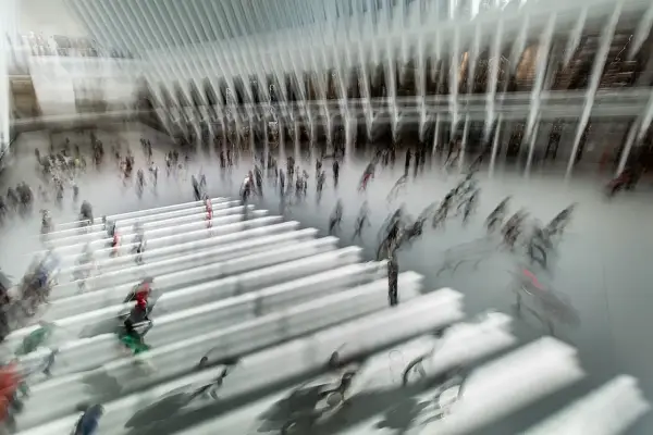 Persone in movimento in una grande hall moderna, con un forte effetto mosso che crea un senso di dinamismo e velocità.